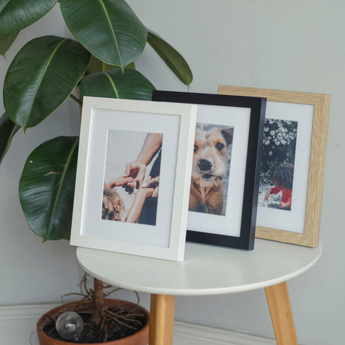 3 photo frames in white, black and oak colours sat on a table